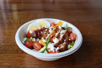 A bowl of salad topped with glazed chicken, feta, and grape tomatoes