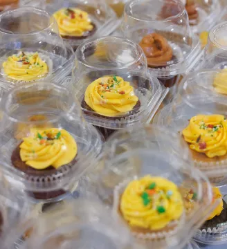 An assortment of yellow frosted cupcakes in individual containers