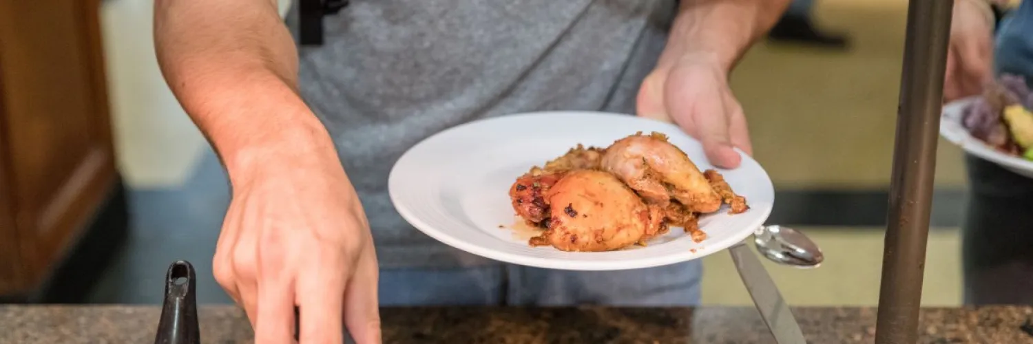 A student serving BBQ chicken onto a plate