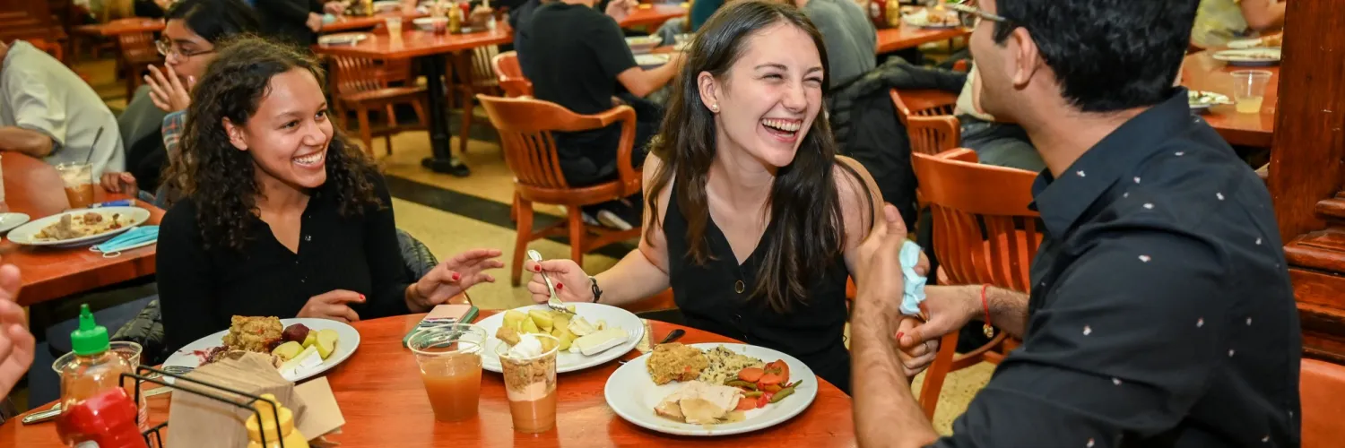 Three students laughing while eating in the dining hall
