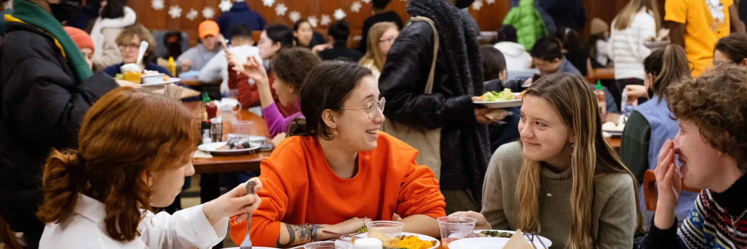 Four students laughing while eating in the dining hall